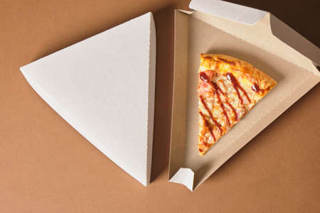 a slices of pizza in a cardboard box in the shape of a triangle for serving and take away, fast food restaurant or pizzeria concept, brown backgroundの写真素材