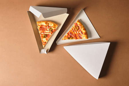 a slices of pizza in a cardboard box in the shape of a triangle for serving and take away, fast food restaurant or pizzeria concept, brown backgroundの写真素材
