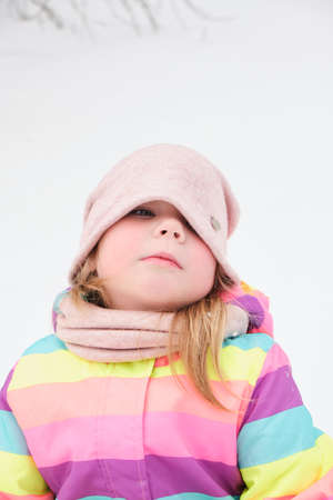 cheerful cute girl 5 years old plays in the snow and makes funny faces, childk in winter in a bright striped suitの写真素材