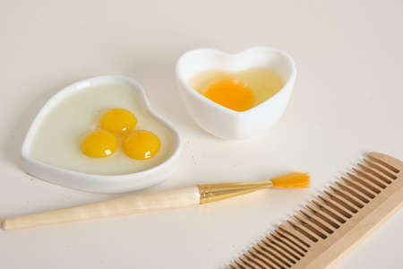 egg-based face, hair and body mask, DIY natural cosmetics concept, comb, brush and raw egg in a heart-shaped bowlの写真素材