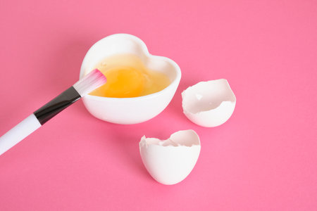 egg-based face, hair and body mask, DIY natural cosmetics concept, shell, brush and raw egg in a...