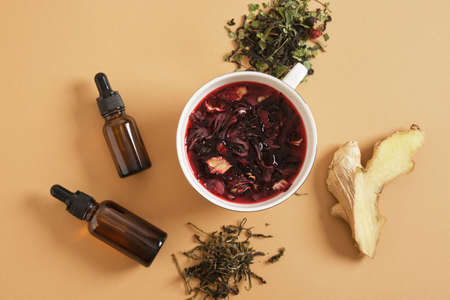 ginger, hibiscus brewed tea in a cup and two dropper bottles with pipettes, stress-reducing supplements, calming drinks top view biege backgroundの写真素材
