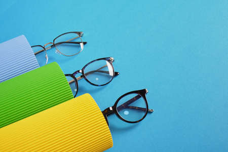 corrugated cardboard rolls and several pairs of stylish glasses, eyeglass frames in fashion trend, bright colors, blue backgroundの写真素材