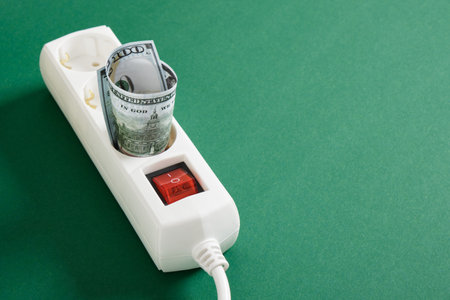 bills of dollars in a surge protector on a green background, an electricity bill concept, a rise in...