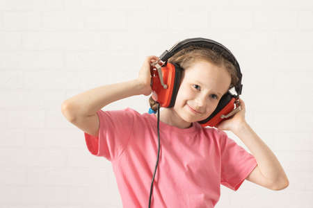Cute happy a girl is listening to music in retro headphones. schoolgirl in headphones and pink...
