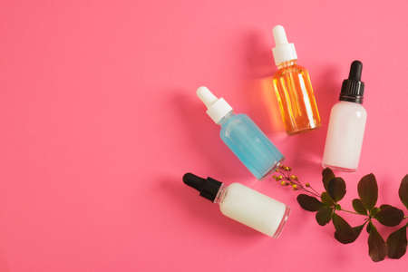 cosmetic serum of different colors for skin care in a transparent dropper bottle on a bright pink background mock-up copy space plant branchの写真素材