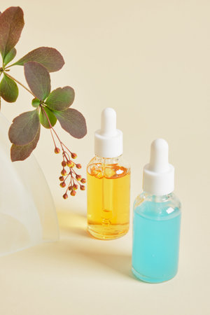 blue and orange serums in transparent dropper bottles and a branch with green leaves and flower buds...