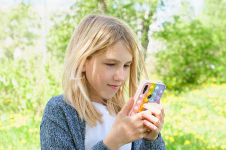 portrait cute teen girl with a smartphone in her hands against the background of summer nature, pop it a phone caseの写真素材