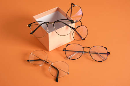 pairs of stylish glasses, eyeglass frames in fashion trend, bright color eye glasses on gift box orange background copy spaceの写真素材