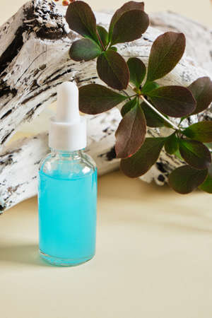 blue serum in a transparent dropper bottle on the background of a wooden snag and branches biege backgroundの写真素材