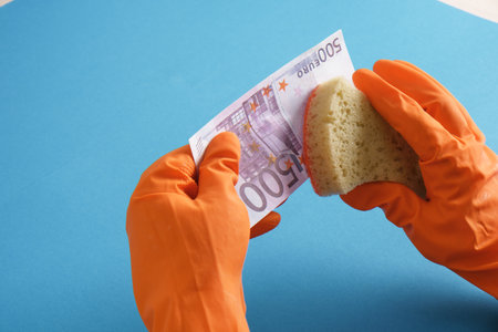 hands in orange gloves wash a 500 euro banknote with soap and a sponge on a blue background dirty moneyの写真素材