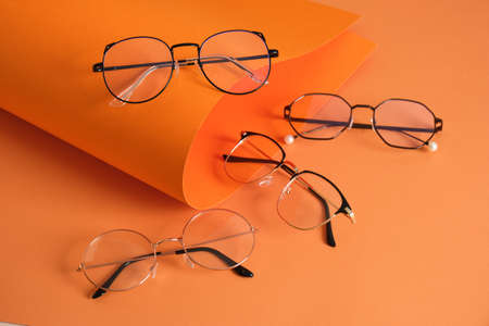 rolles orange paper and several pairs of stylish glasses, eyeglass frames in fashion trend, bright colors, orange backgroundの写真素材