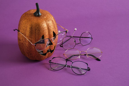trendy stylish glasses and the face of a decorative shiny orange pumpkin on a purple background copy spaceの写真素材