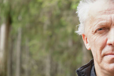 Close up of senior man half face in forest. Copy space in left side.