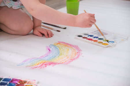 kid painting rainbow, little girl painting colorful rainbow on large sheet of paper, watercolorsの写真素材