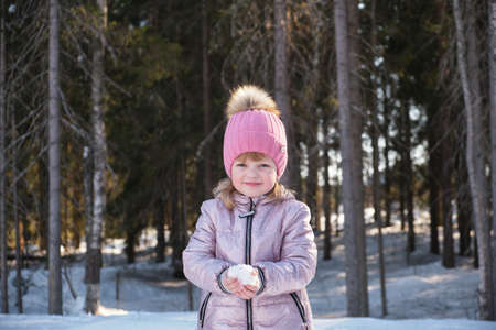 cute girl in a hat and jacket has fun with snow, winter sunny weather, snowflakes in her palms,...