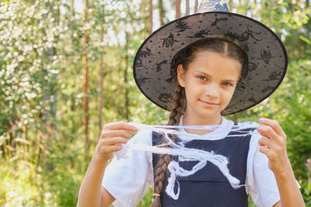 cute funny teen girl playing with decorative web, halloween preparation, traditional costume with cap, witch or wizardの写真素材