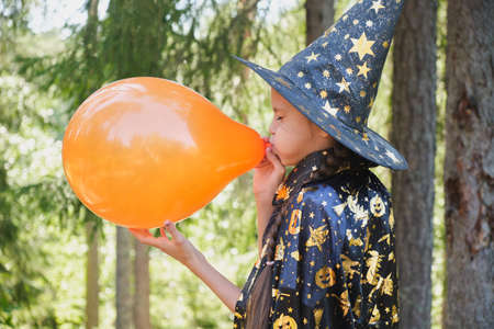 a cheerful girl with pigtails inflates a balloon for decoration of a halloween party, a fun halloween, a girl in a wizard or witch costumeの写真素材