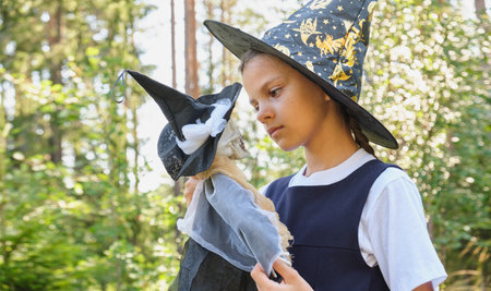 cute funny teen girl playing in decorative skeleton for halloween holiday decoration, witch costume with masquerade capの写真素材