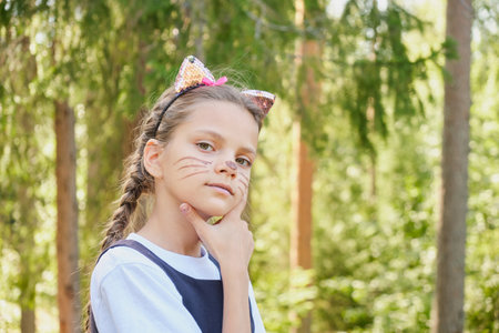 cheerful teenage girl in a costume for the celebration of halloween, a costume party in nature, a child in a cat costume with ears and a painted mustacheの写真素材