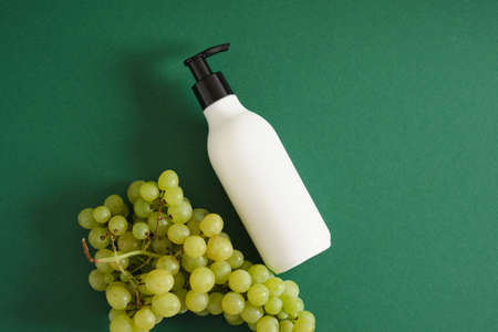 white mock up bottle with dispenser and grapes on green background natural cosmetic concept, top view copy spaceの写真素材