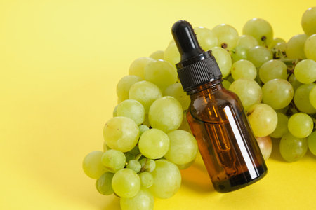 amber glass droppe bottle and green grapes on yellow background, natural cosmetic concept mock up copy spaceの写真素材