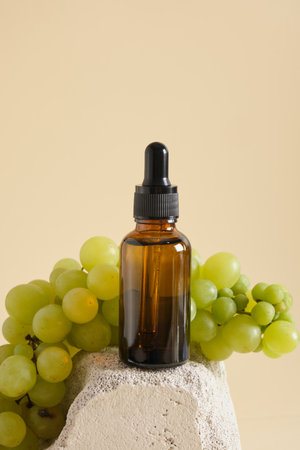 amber glass droppe bottle and green grapes on a concrete podium a yellow background, grape seed cosmetics, oils and serums in a bottle with a pipetteの写真素材