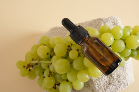 amber glass droppe bottle and green grapes on a concrete podium a yellow background, grape seed cosmetics, oils and serums in a bottle with a pipetteの写真素材
