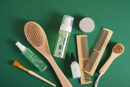 Women hair care set. Comb, wooden brush, gel, jar, dropper bottle and yellow flowers on green background top viewの写真素材