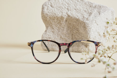 trendy fashion eyeglasses on concrete podium and Gypsophila flowers on beige background, creative...