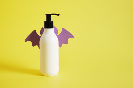 mockup bottle with dispenser with oil or cream with bat wings, yellow background, cosmetics and halloweenの写真素材