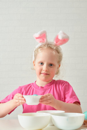 little girl in bunny ears , Easter concept, table with Easter eggs, celebrating Easter. child paints...