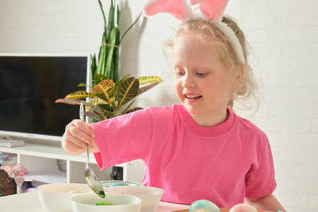 little girl in bunny ears , Easter concept, table with Easter eggs, celebrating Easter. child paints easter eggs at homeの写真素材