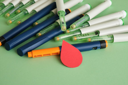 Diabetes concepta a paper drop of blood and a lot of syringe pens with insulin on a green backgroundの写真素材
