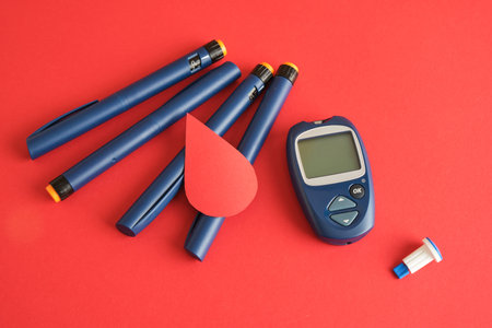 Diabetes concepta a device for measuring blood sugar, a paper drop of blood and syringe pens with insulin on red backgroundの写真素材