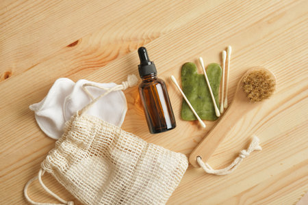 jade gouache scraper, massage oil in a glass amber bottle with a pipette, massage brushes and cotton sponges on a wooden background, reusable wicker bagの写真素材