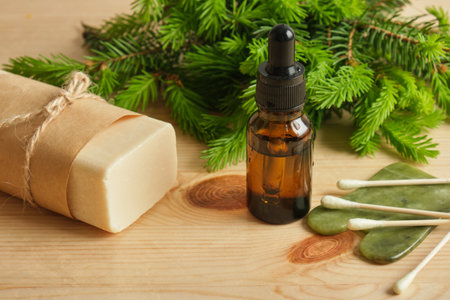soap, glass amber bottles with pipettes and spruce branches with young needles on a wooden background, useful properties of young spruce shoots, massage oil and gua shaの写真素材