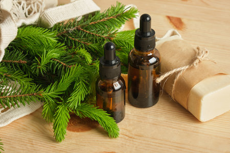 soap, glass amber bottles with pipettes and spruce branches with young needles in a mesh bag on a wooden background, useful properties of young spruce shootsの写真素材