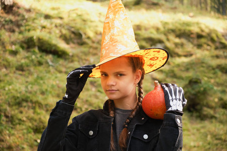portrait of a teenage girl in an orange pointed hat and holding a pumpkin in her hands against the...