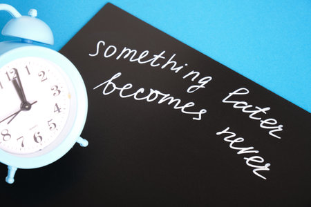 something later becomes never chalk marker writing on black board and alarm clock, concept of...