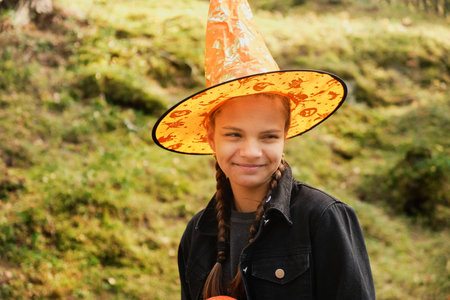 portrait of teenage girl in orange pointed hat against nature background, halloween conceptの写真素材