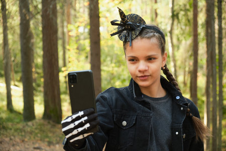girl in witch or wizard costume for halloween party having fun and taking selfie on her smartphone...