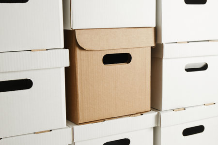 one brown box and a pile of white cardboard boxes with slots for holding, storage boxes, wall of...