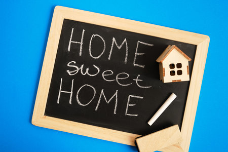 small wooden house, black chalk board with home sweet home inscription on blue backgroundの写真素材