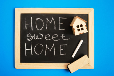 small wooden house, black chalk board with home sweet home inscription on blue backgroundの写真素材