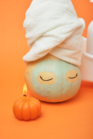 Halloween candle and pumpkin with eyes and a white terry towel on the head, a blue clay mask on the face, orange backgroundの写真素材