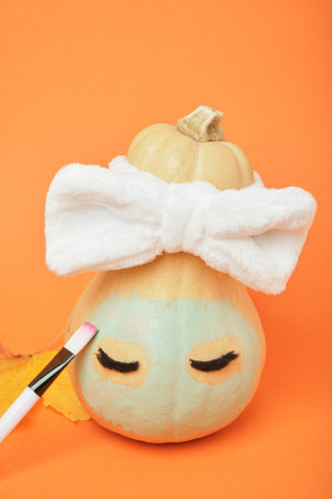 Autumn pumpkin with clay mask in white cosmetic bandage on orange background, brushes for applying mask, copy space, mock upの写真素材