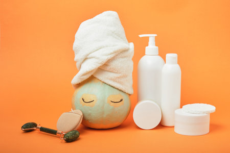 Pumpkin with face and towel in clay mask on orange background, natural cosmetics concept, autumn skincare routineの写真素材