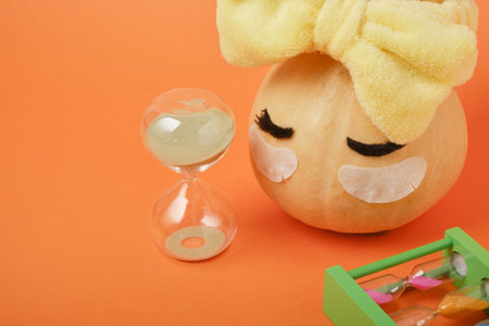 Autumn pumpkin with gray clay mask in yellow cosmetic bandage and hourglass on orange background, copy space, mock up, self-care time conceptの写真素材