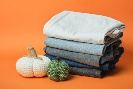 Decorative pumpkin and stack of jeans of different colors on orange background, autumn clothing sale conceptの写真素材